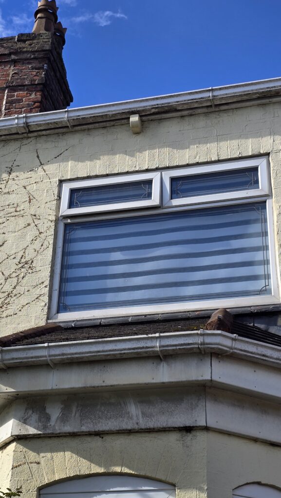 Dirty guttering and fascia above a bay window before exterior cleaning and painting during an ivy removal project in Greater Manchester.